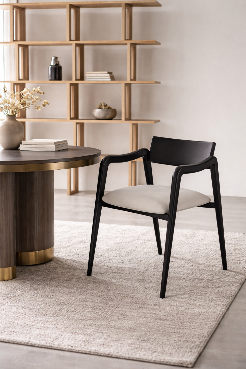 Dining room with a round wooden table and black chair, wooden shelf in the background.