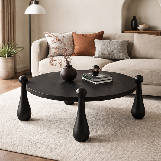 Round black coffee table with unique legs in a living room setting.