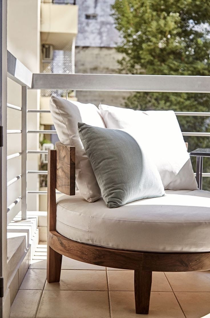 Rustic Round wooden outdoor chair with white cushions and a green pillow on a balcony.