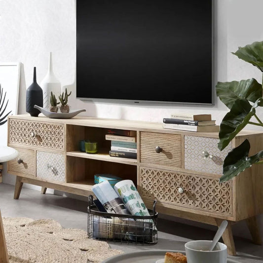 A carved wooden TV cabinet with open and closed shelves, Shown with a flat-screen TV on top, books, magazines, and decorative items on the shelves, placed in a living room setting.