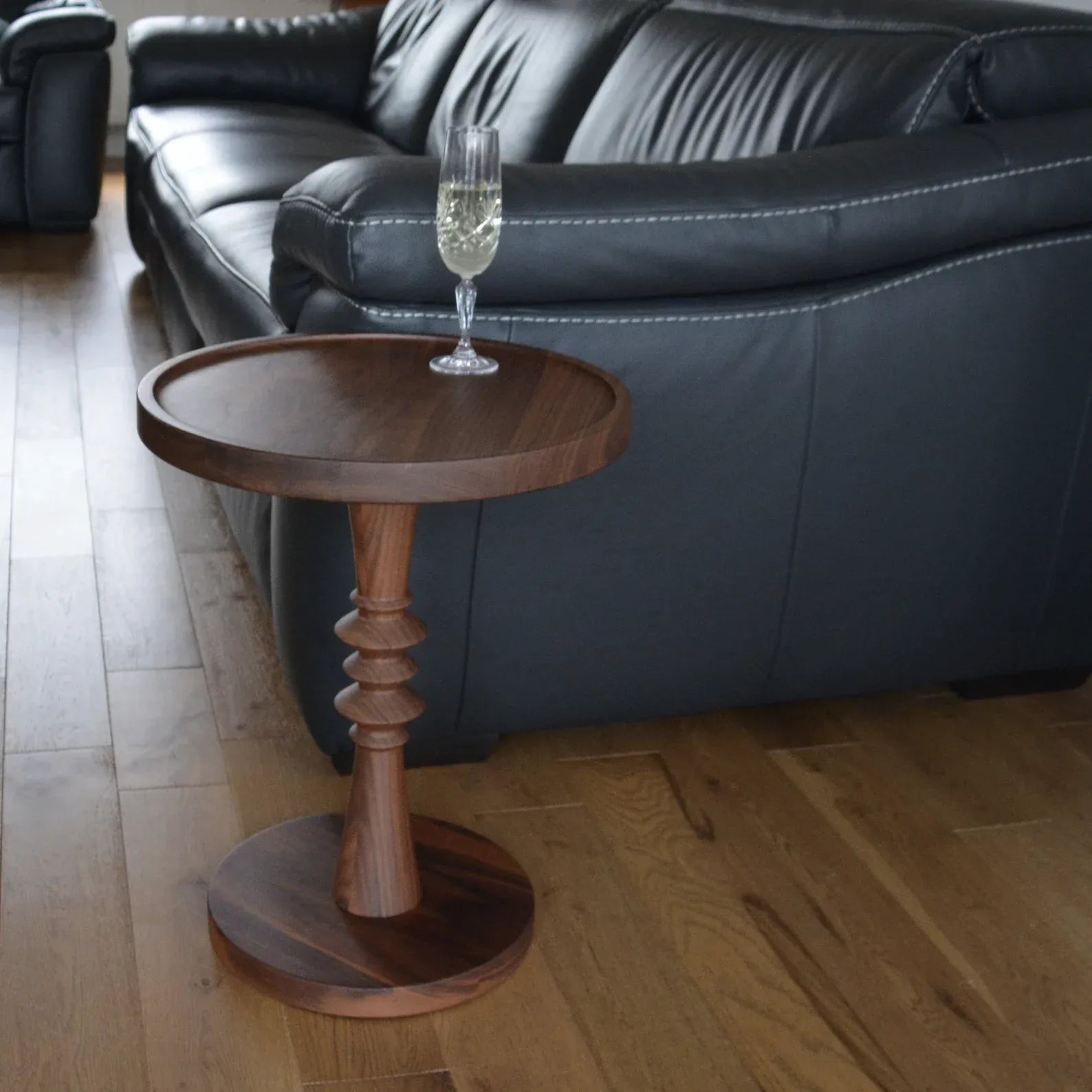 Wooden side table with a glass of champagne in front of a black leather sofa.