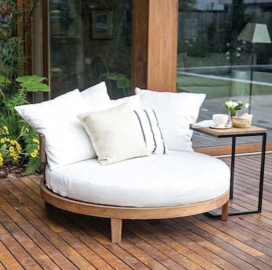Round outdoor sofa with white cushions on a wooden deck