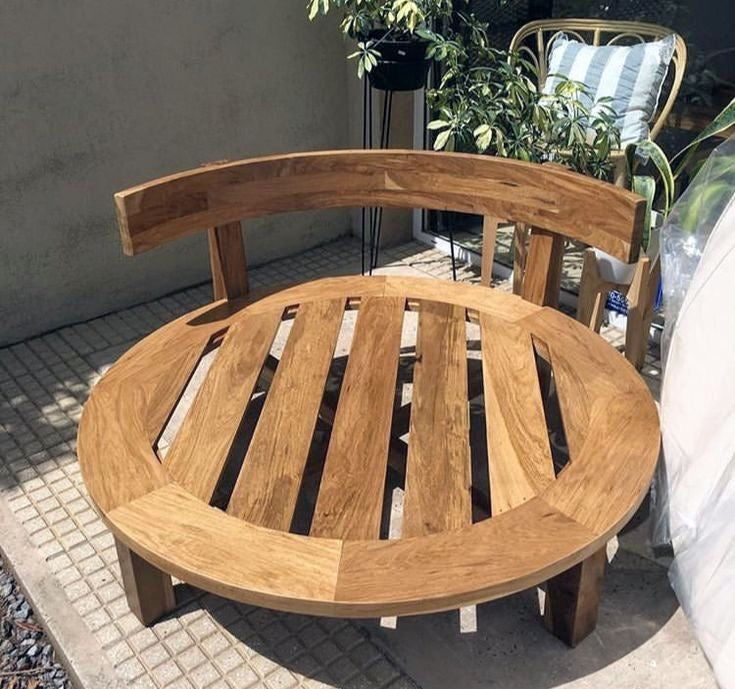 Wooden circular chair on a patio with plants and a gray wall in the background